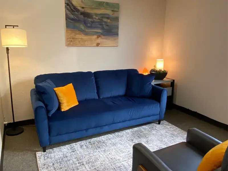 Cozy counseling room featuring a blue sofa with yellow accent pillow, warm lighting, and calming wall art, reflecting SagePoint Behavioral Health's supportive environment for mental health and substance use recovery.