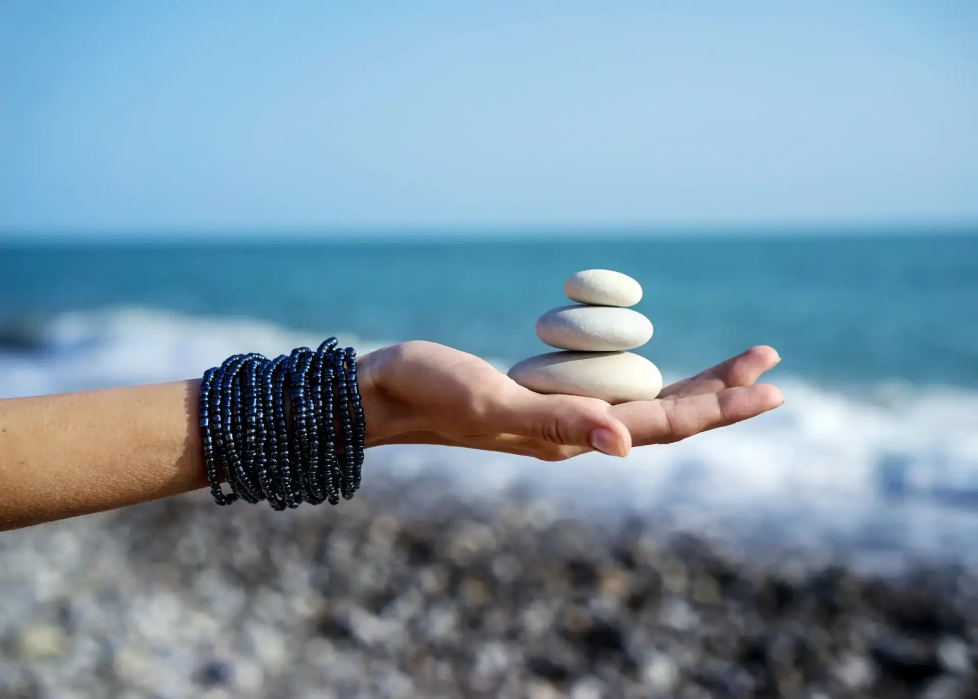 Hand holding balanced stones symbolizing tranquility and mindfulness by the ocean, representing coping strategies for cravings in addiction recovery.