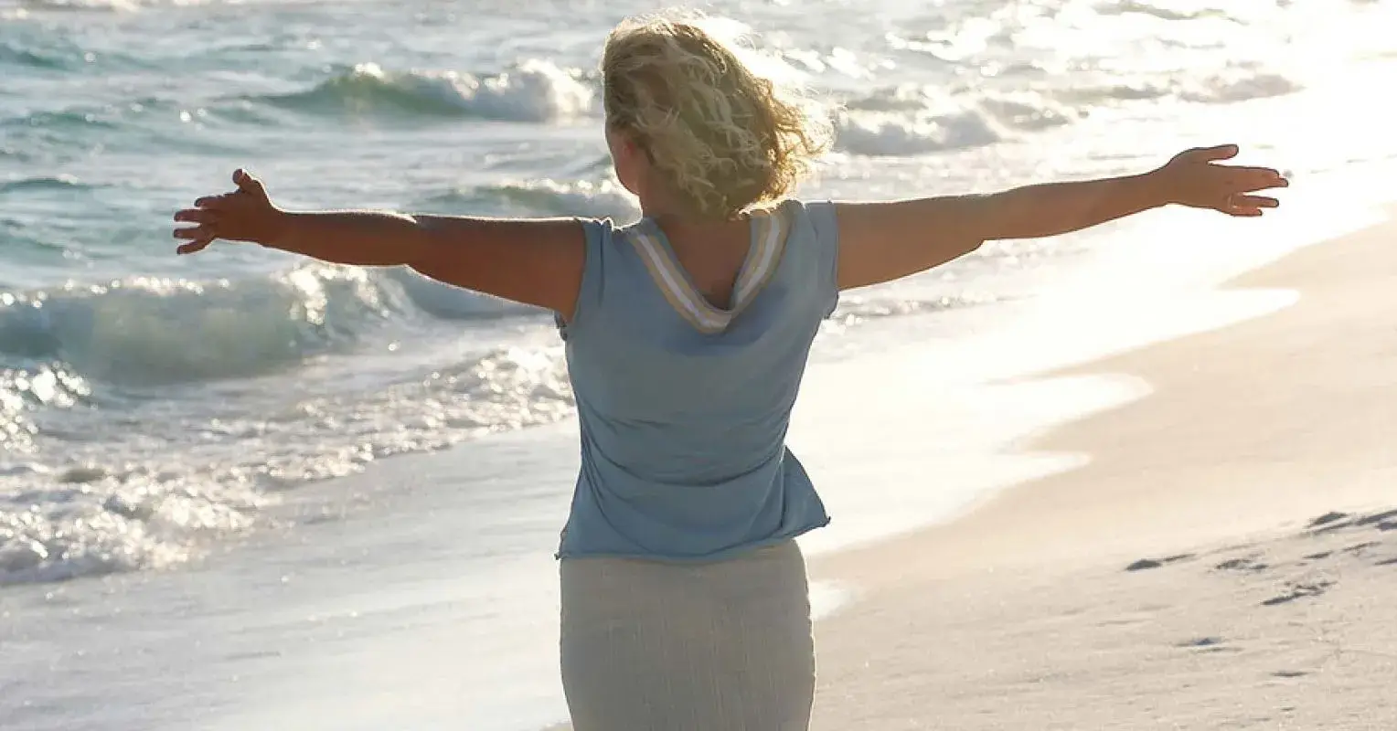 Woman with outstretched arms standing on the beach, embracing freedom and new beginnings, symbolizing recovery from addiction and emotional healing.