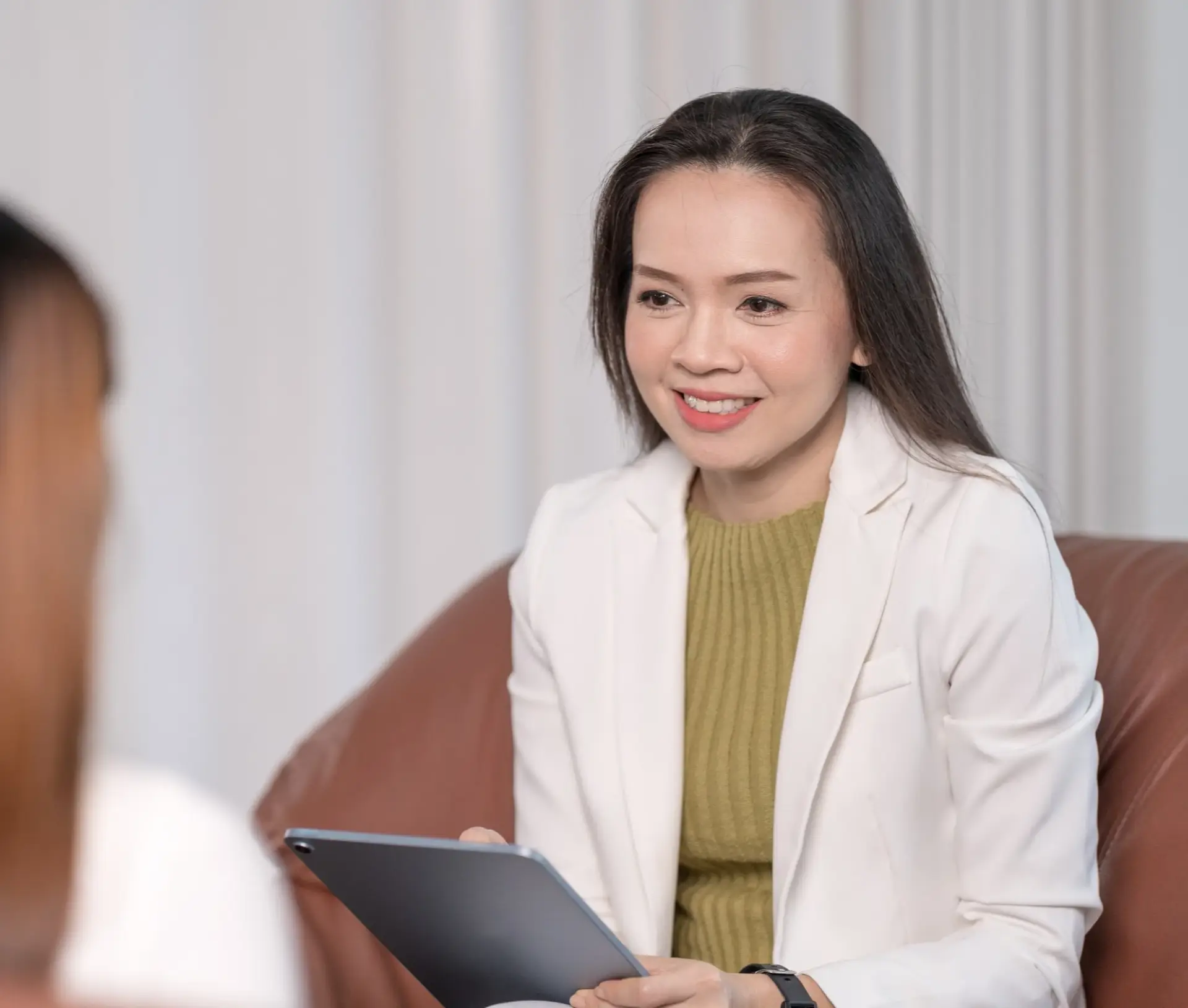 Therapist in white blazer smiling and holding tablet during a counseling session, emphasizing supportive mental health treatment in an Intensive Outpatient Program (IOP).