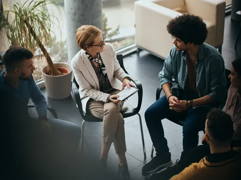 Group therapy session at SagePoint Behavioral Health, featuring a female therapist engaging with clients in a supportive environment, emphasizing mental health and substance use recovery.