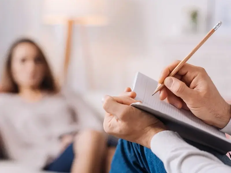 Person writing notes during a case management session with a client in a therapeutic setting, emphasizing mental health support and personalized care coordination.