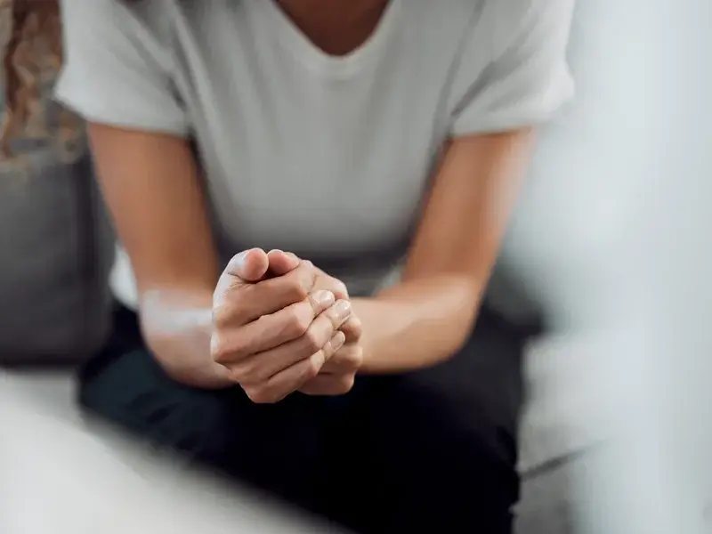 Person with clasped hands, reflecting on mental health challenges, in a therapeutic setting, emphasizing emotional support and recovery.
