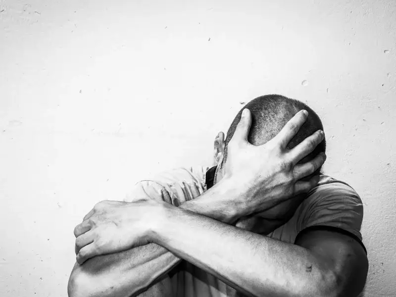 Man with shaved head sitting with his head in his hands, expressing emotional distress, symbolizing the challenges of substance use recovery and the need for supportive treatment at SagePoint Behavioral Health.