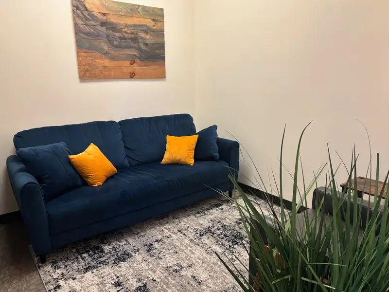 Therapist office at SagePoint Behavioral Health featuring a blue couch with yellow pillows, a decorative wall art piece, and a welcoming atmosphere for mental health and substance use recovery.